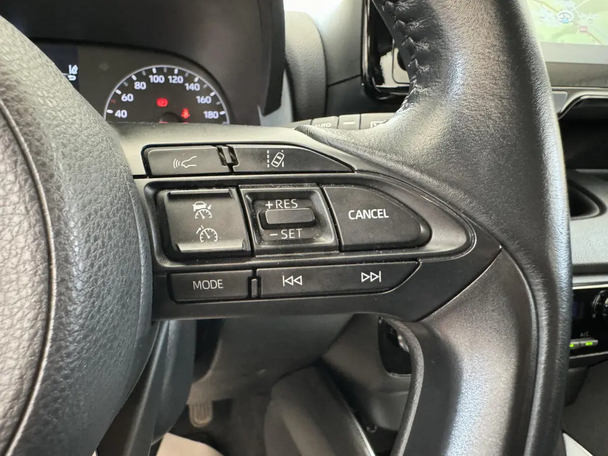 Gros plan sur les commandes au volant cuir noir de la Toyota Yaris hybride 2022, avec tableau de bord et écran tactile visibles.