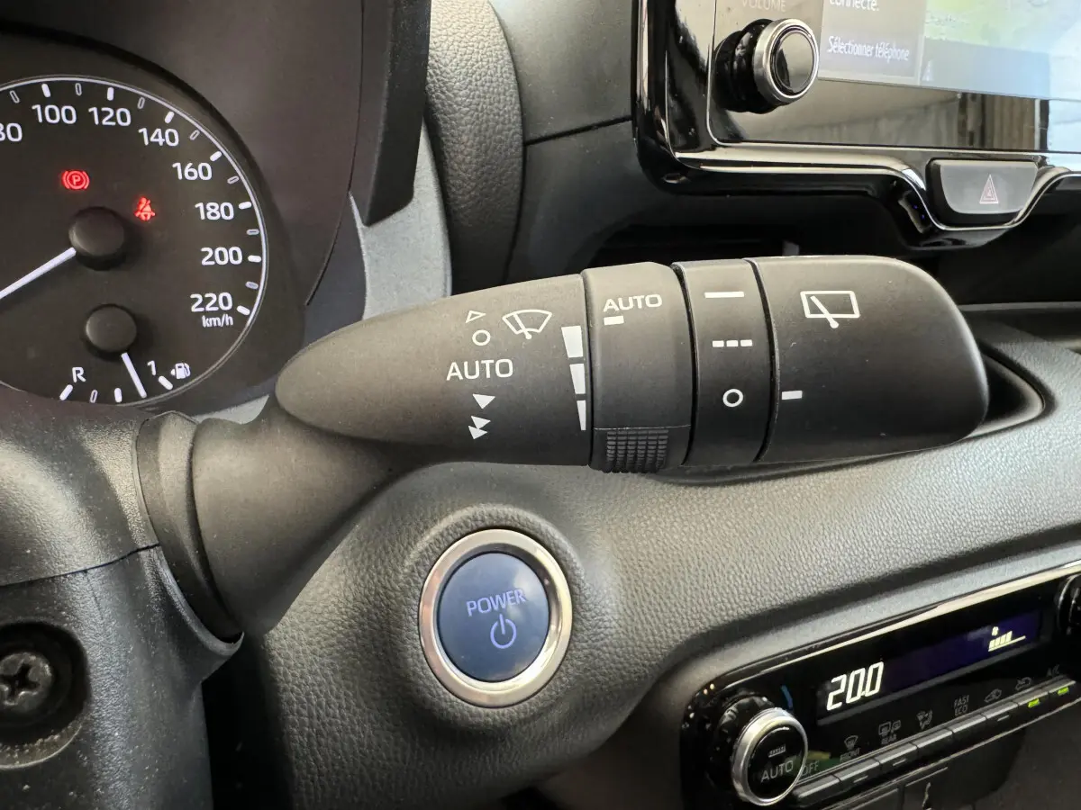 Gros plan sur la commande d’essuie-glace et bouton Power bleu du tableau de bord noir de la Toyota Yaris hybride 2022.