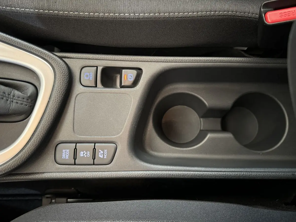 Vue rapprochée de la console centrale noire de la Toyota Yaris hybride avec boutons de modes de conduite et frein à main électrique.