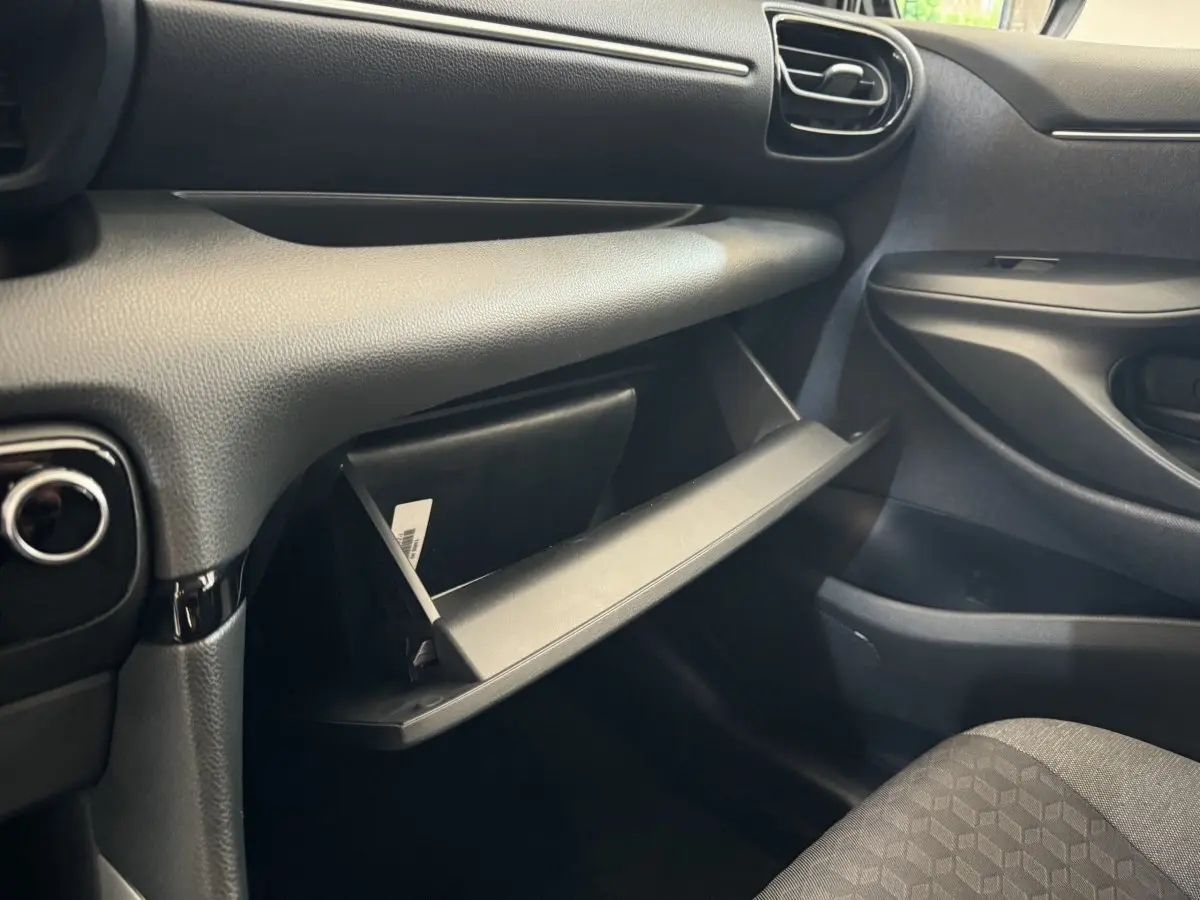 Vue intérieure côté passager de la Toyota Yaris hybride 2022, boîte à gants ouverte et sièges gris visibles.