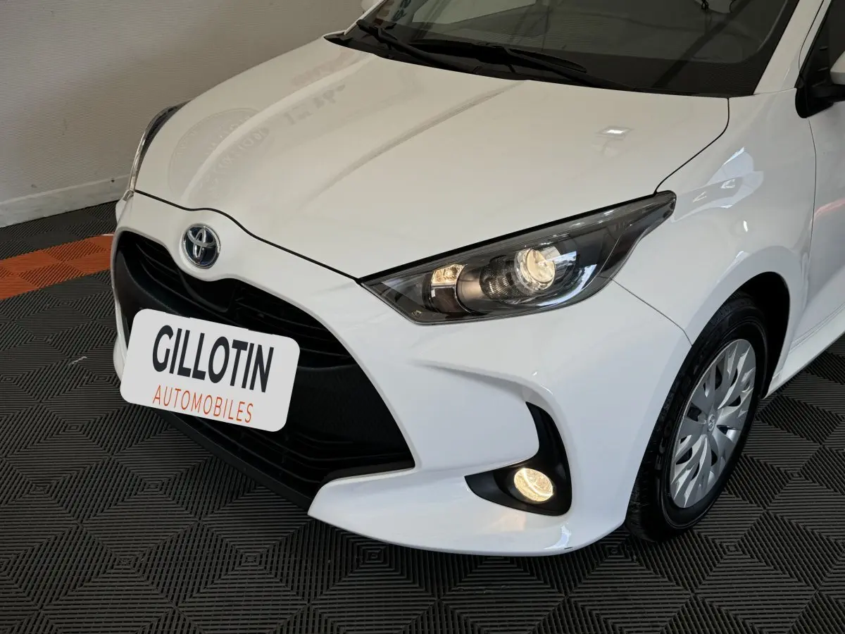Vue 3/4 avant droit d'une Toyota Yaris blanche avec phares allumés et calandre noire distinctive.