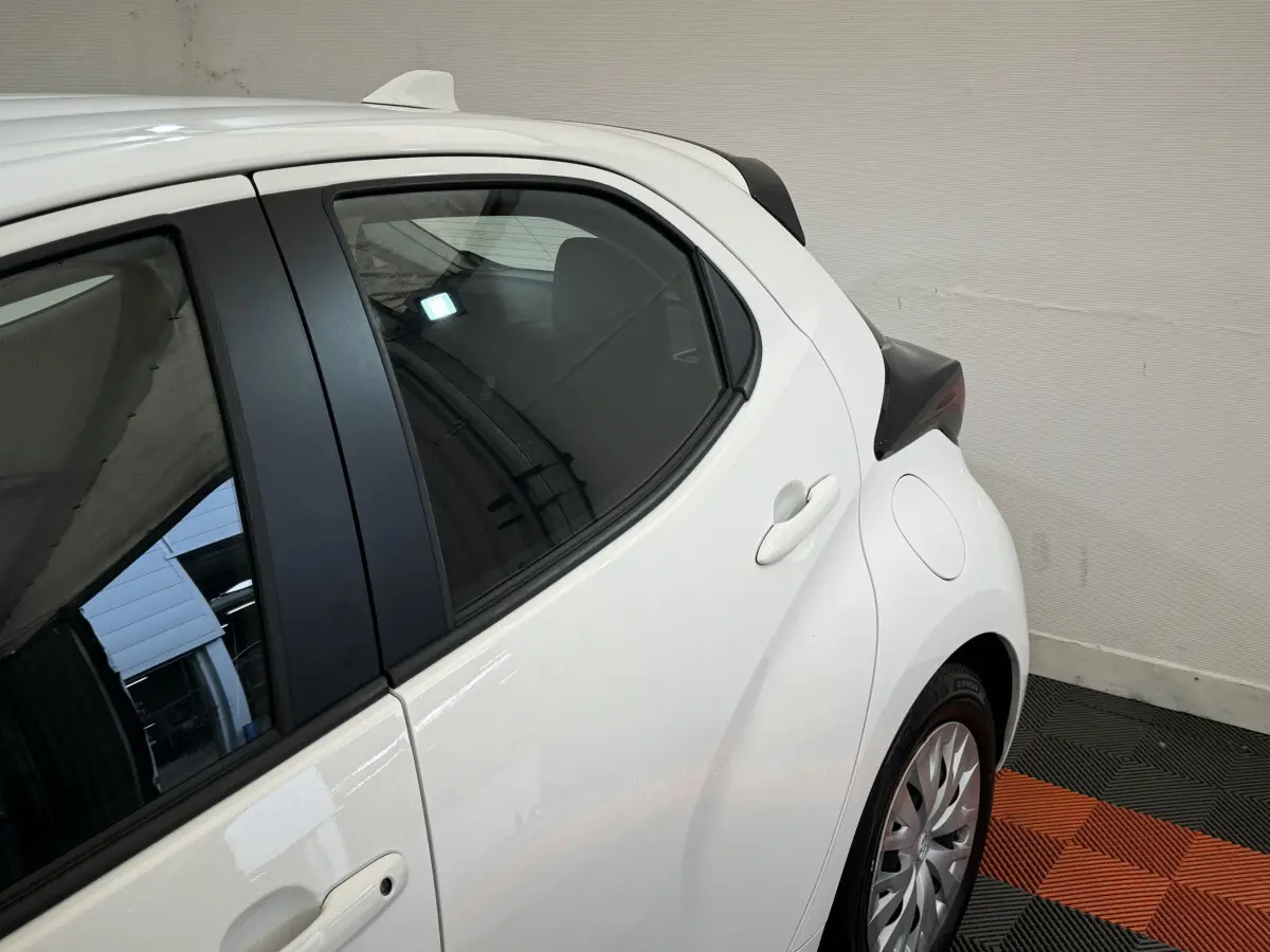 Vue côté droit arrière de la Toyota Yaris hybride blanche 2022, mettant en valeur la porte arrière et le passage de roue.