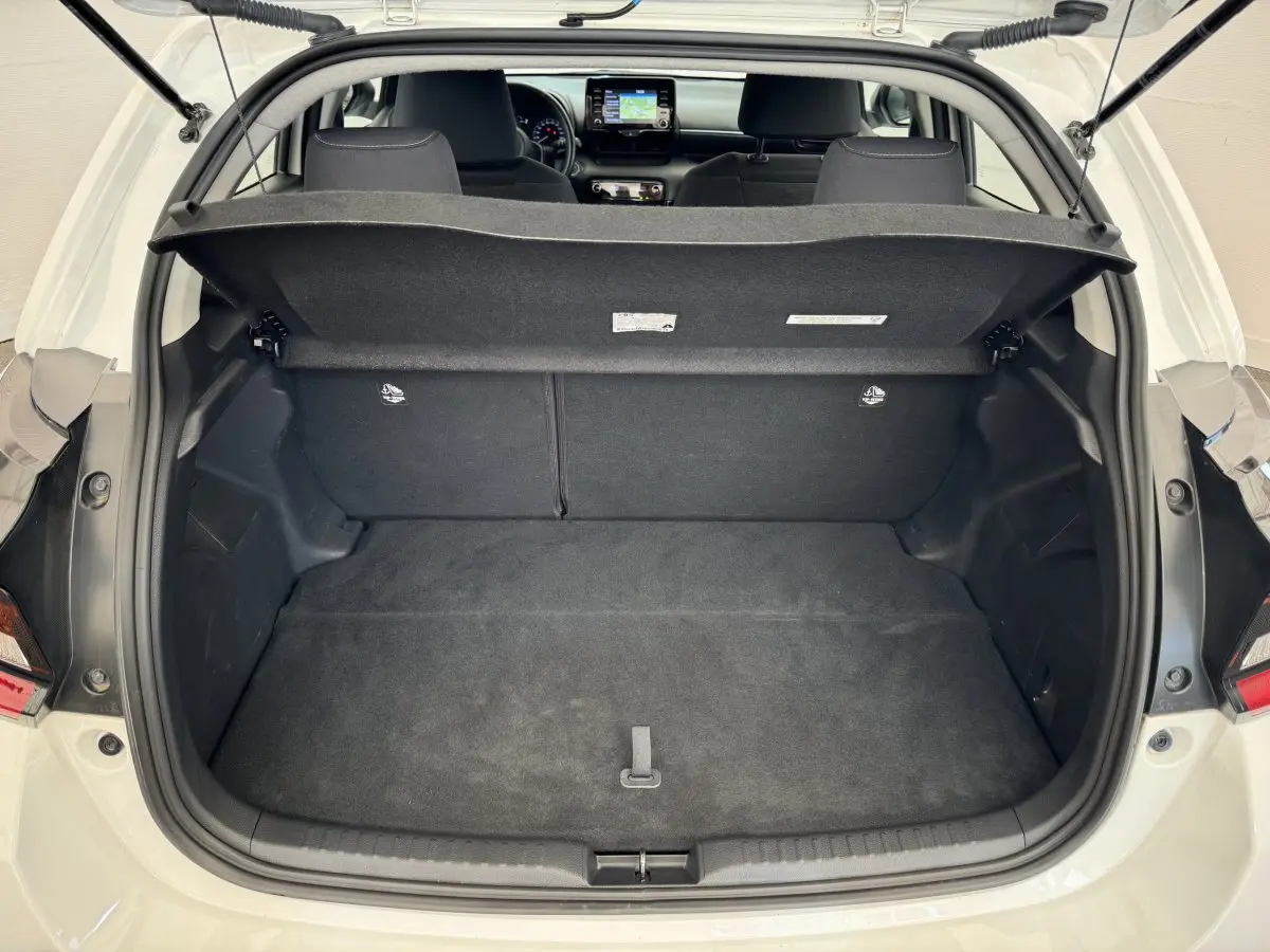 Coffre ouvert d'une Toyota Yaris hybride blanche 2022, vue arrière montrant l'intérieur spacieux et la tablette de coffre relevée.