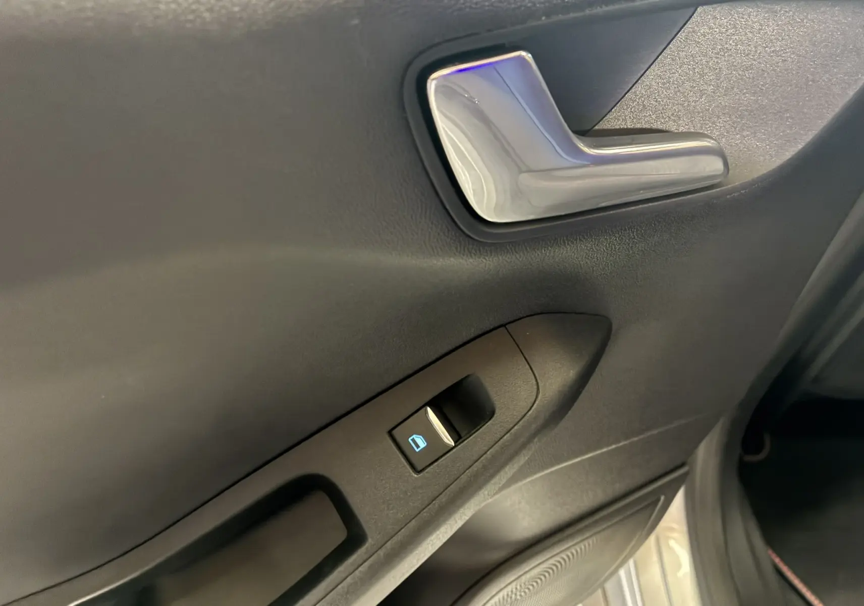 Poignée de porte intérieure gris foncé avec bouton de commande de vitre sur une Ford Fiesta 2020 côté gauche.