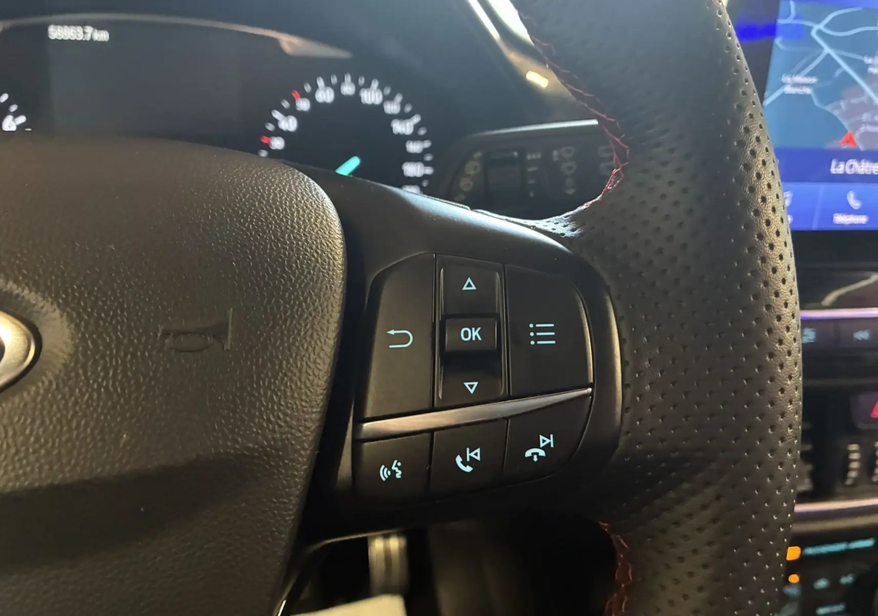 Gros plan sur les commandes multifonctions à droite du volant perforé d'une Ford Fiesta gris 2020, avec tableau de bord et écran GPS en arrière-plan.