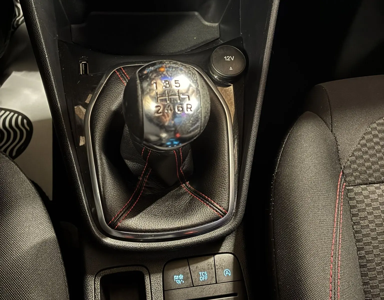 Gros plan sur le levier de vitesses manuel noir avec surpiqûres rouges dans une Ford Fiesta gris 2020, intérieur tissu noir.