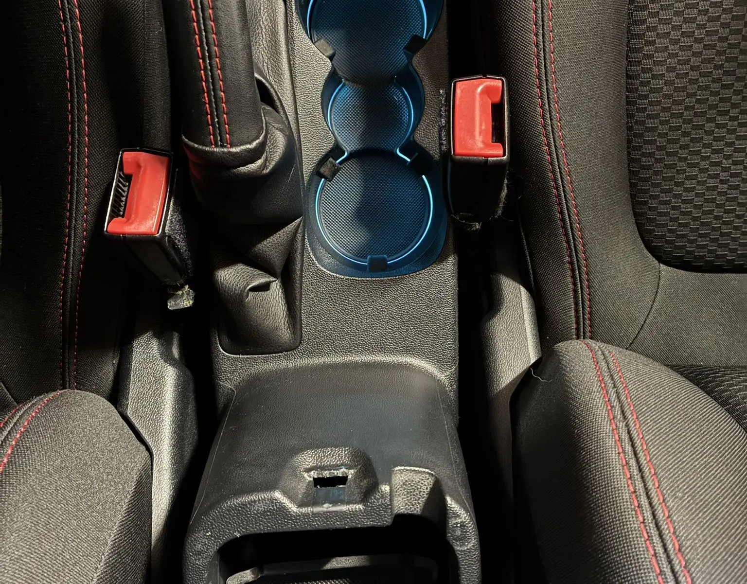 Vue plongeante sur la console centrale intérieure de la Ford Fiesta gris, avec levier de frein à main et porte-gobelets bleutés.