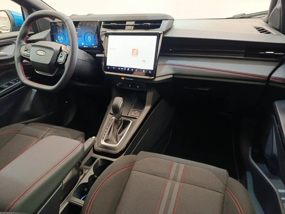 Intérieur Ford Puma 2025 vu côté conducteur, tableau de bord noir avec écran tactile central et coutures rouges sur sièges.