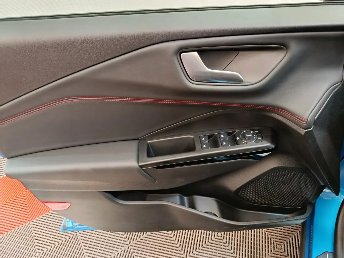 Porte côté conducteur du Ford Puma bleu 2025, intérieur noir avec surpiqûres rouges et commandes électriques.