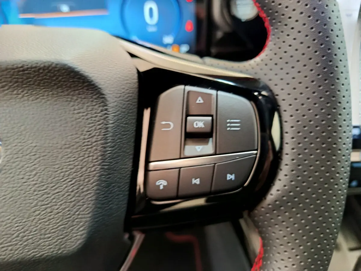 Gros plan sur les commandes multifonctions à droite du volant perforé noir avec surpiqûres rouges du Ford Puma bleu 2025.