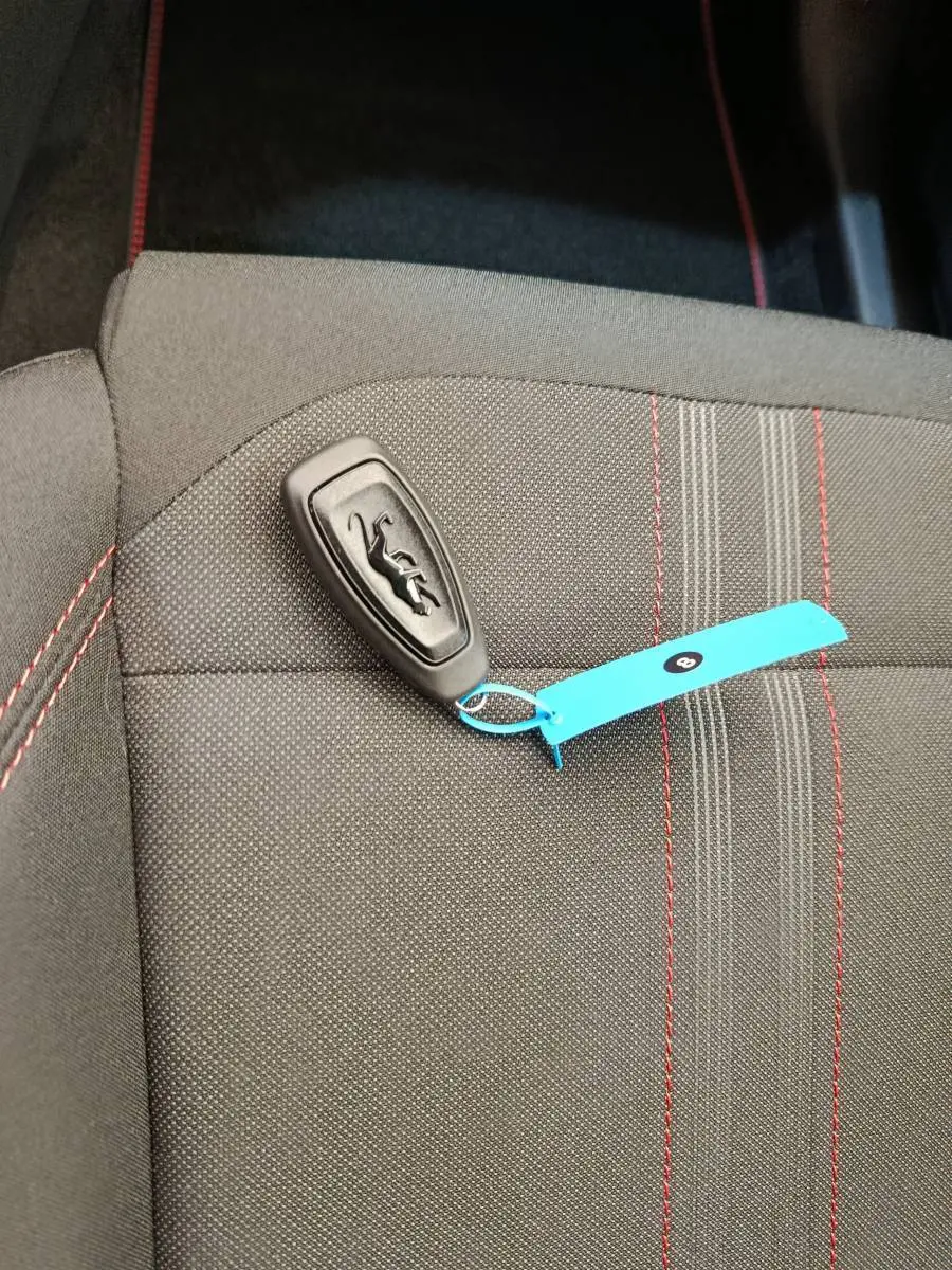 Gros plan sur une clé Ford posée sur un siège tissu gris foncé avec surpiqûres rouges, intérieur du Ford Puma.