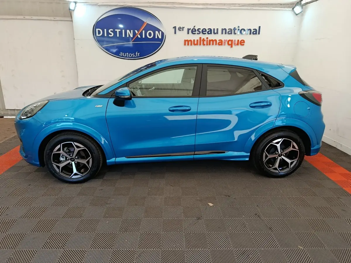 Profil côté gauche d'un Ford Puma bleu 2025 ST-LINE avec jantes alliage et toit noir en showroom.