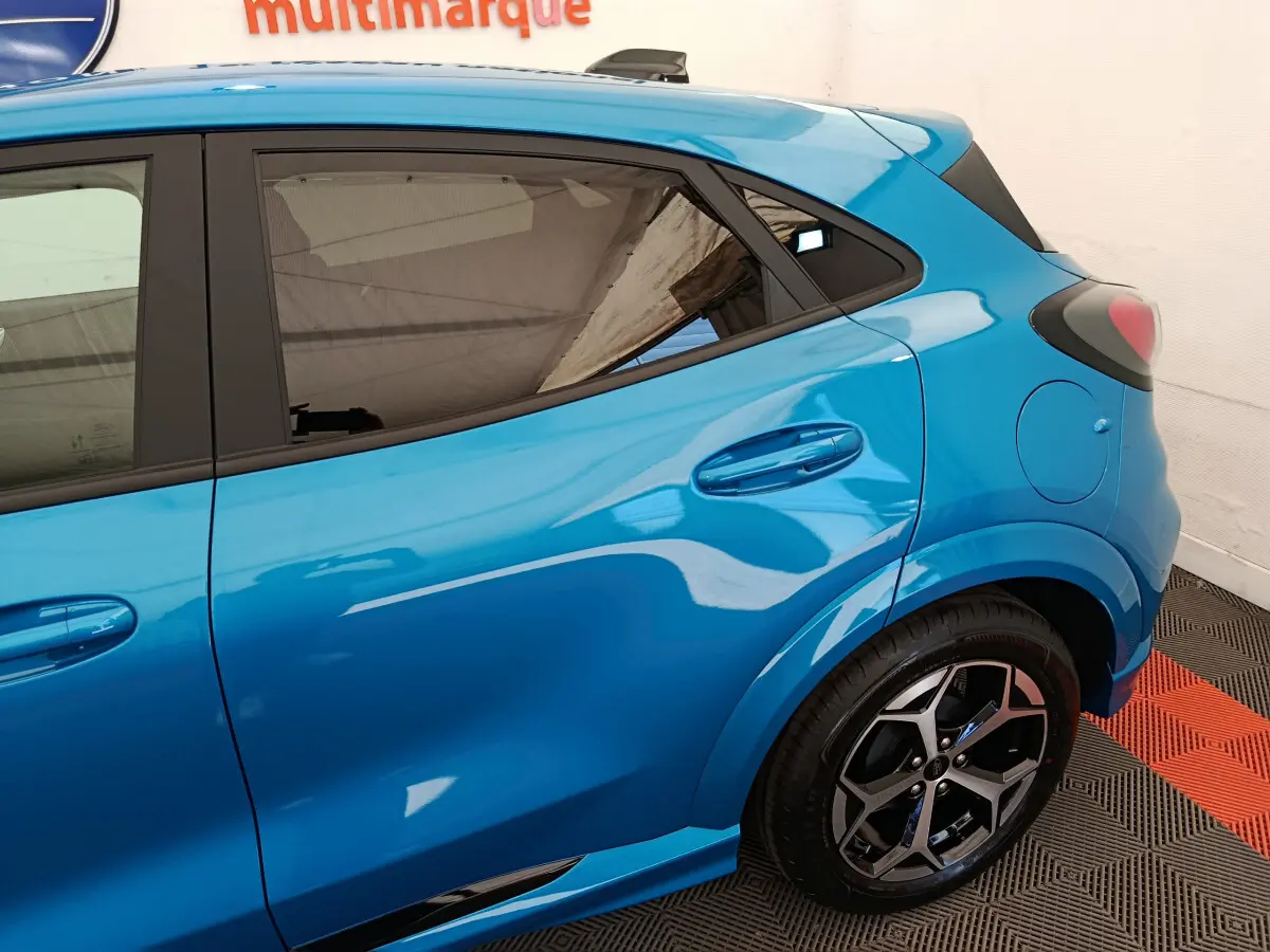 Vue côté droit arrière du Ford Puma bleu 2025 avec jante alliage et vitres teintées dans un showroom.