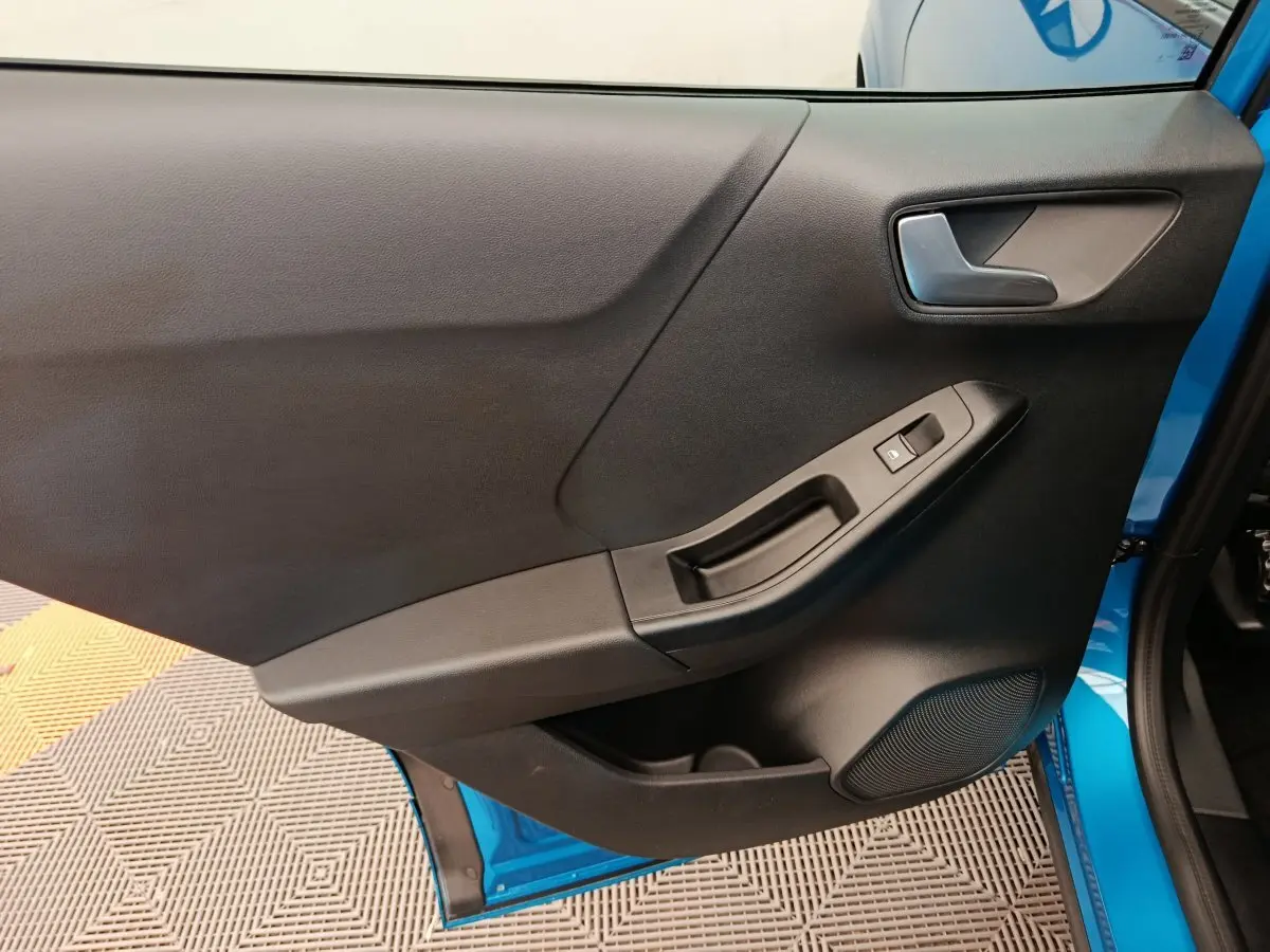 Vue rapprochée de la porte avant droite noire du Ford Puma bleu 2025, avec commande de vitre et poignée intégrée.