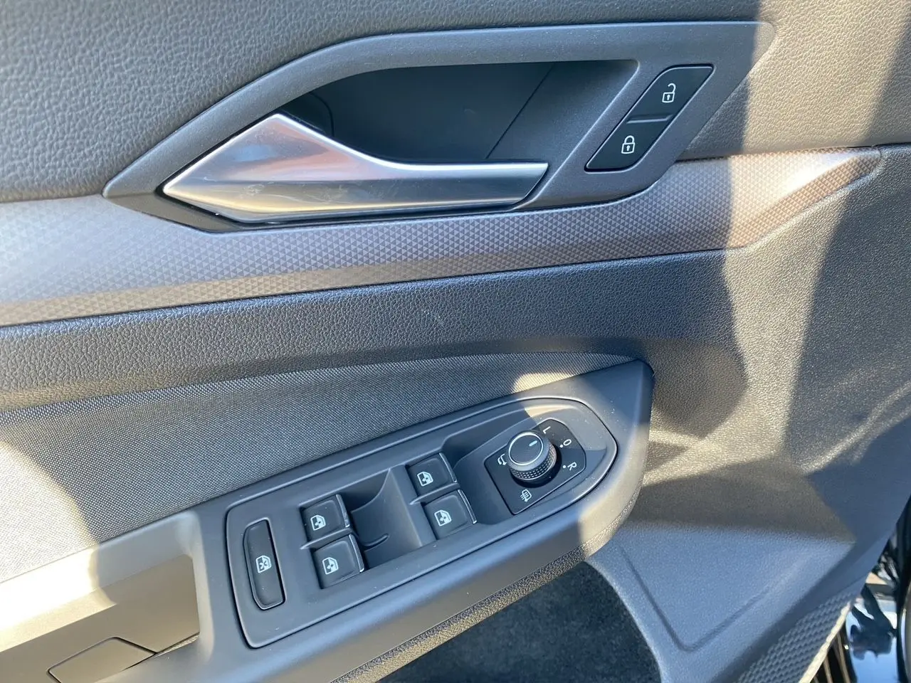 Détail de la porte côté conducteur d'une Volkswagen Golf VIII noire, montrant les commandes des vitres et rétroviseurs.