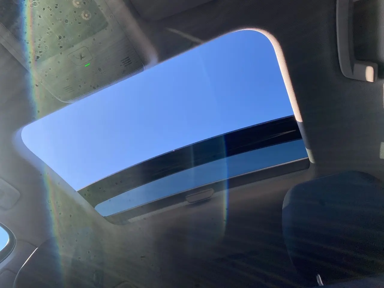 Vue intérieure du toit panoramique ouvert de la Volkswagen Golf VIII noire, laissant apparaître un ciel bleu lumineux.