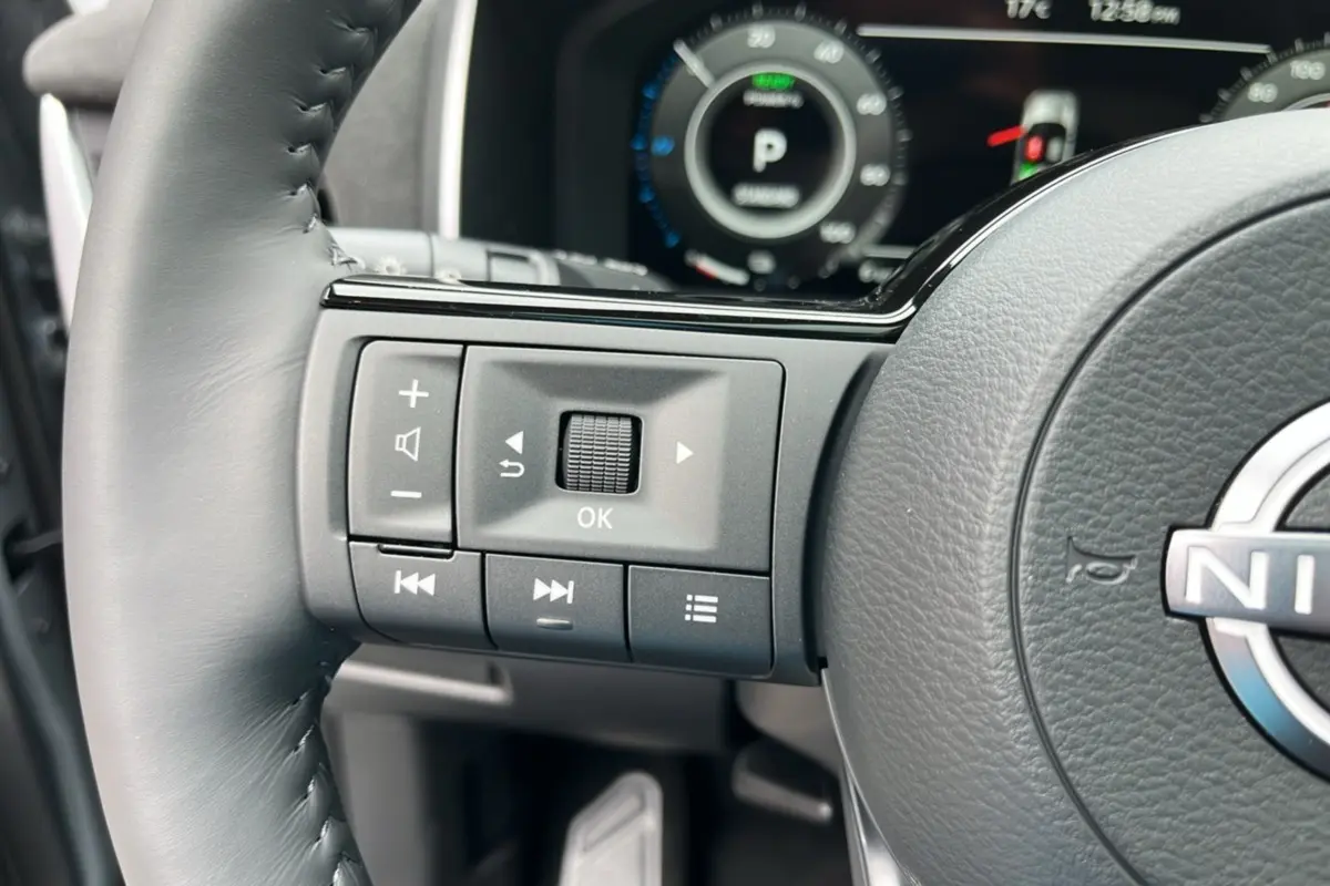 Gros plan sur les commandes gauche du volant cuir noir du Nissan Qashqai E-POWER 205 Tekna Plus avec tableau de bord numérique.