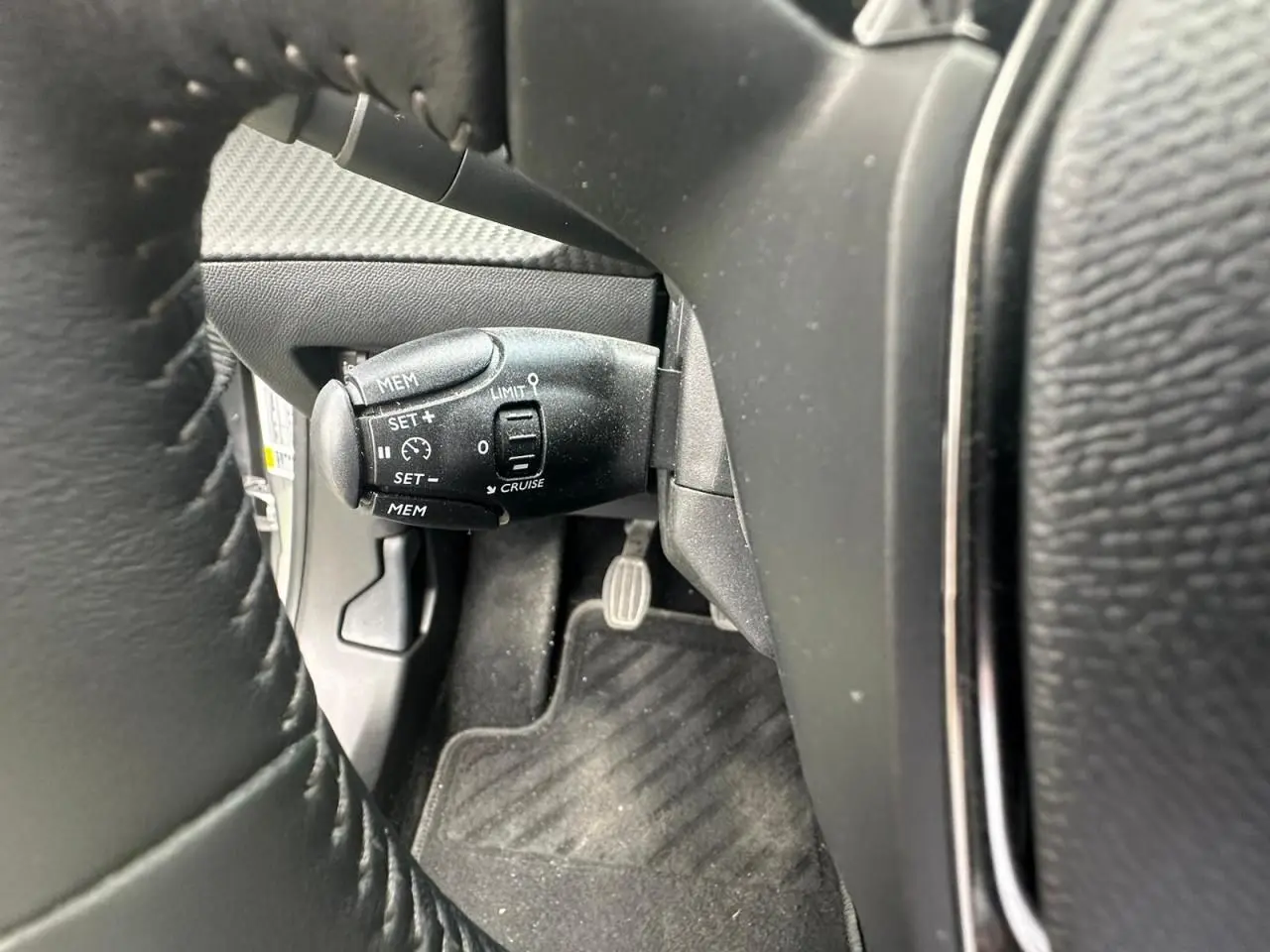 Gros plan sur la commande de régulateur de vitesse noire à gauche du volant cuir du Peugeot 2008 gris clair.