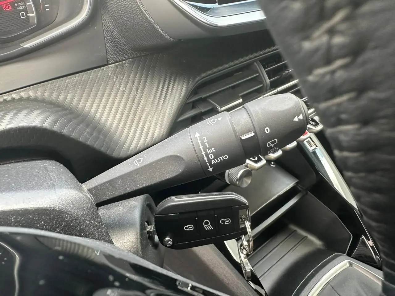 Gros plan sur la commande d'essuie-glace et la clé insérée dans le contacteur d'une Peugeot 2008 gris clair.