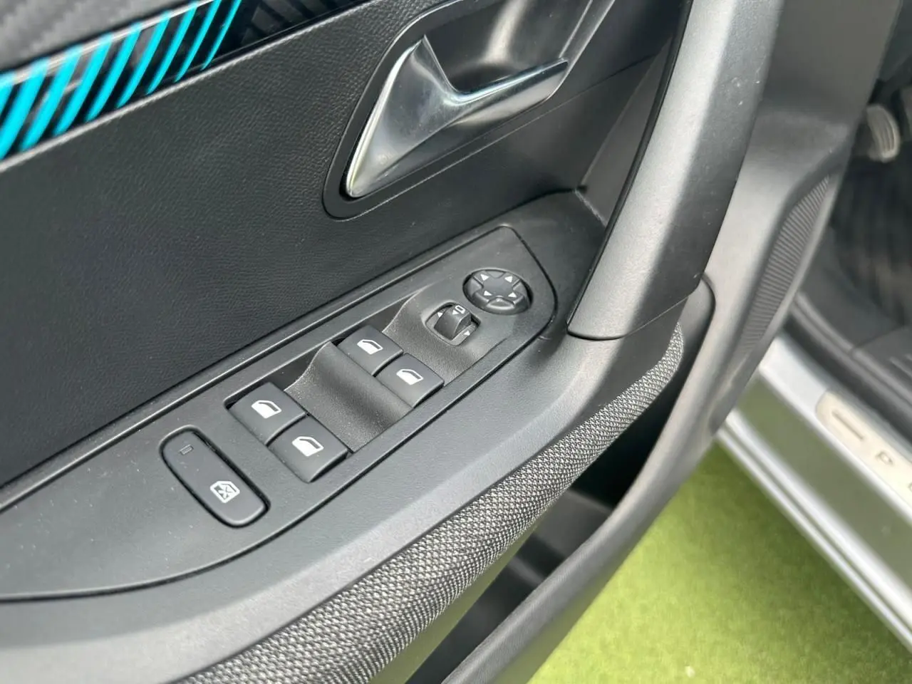 Détail de la commande des vitres électriques côté conducteur d'une Peugeot 2008 gris clair, avec insert bleu sur la porte.