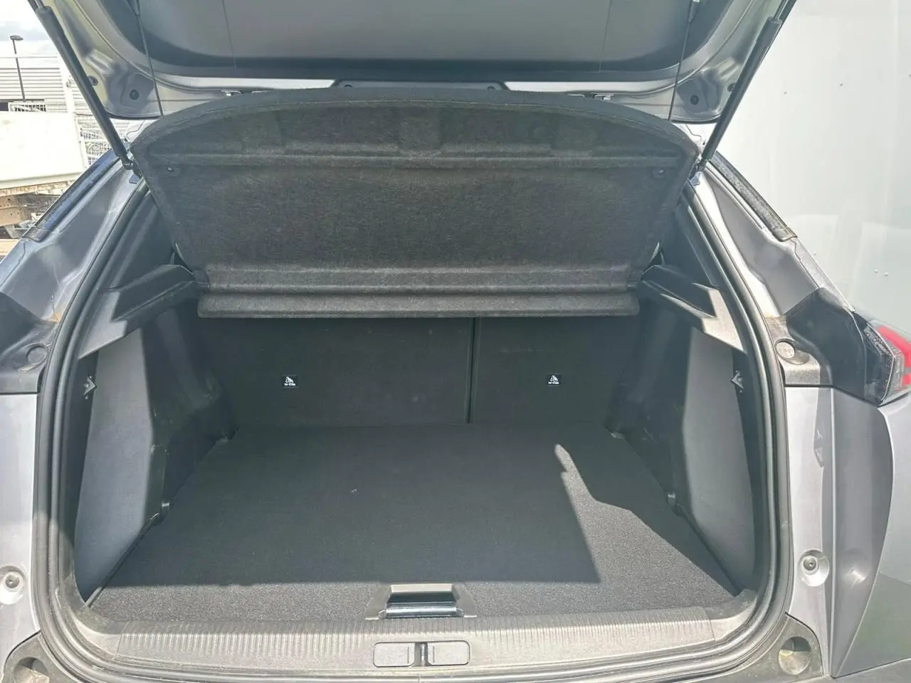 Coffre ouvert d'un Peugeot 2008 gris clair vu de l'arrière, montrant l'espace de chargement vide et la tablette cache-bagages relevée.