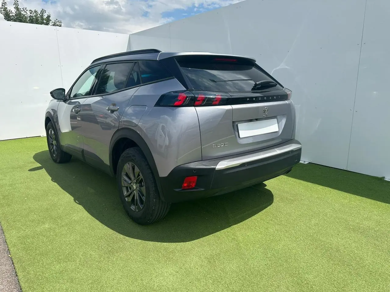 Vue 3/4 arrière droite du Peugeot 2008 gris clair avec feux arrière LED et barres de toit noires brillantes.