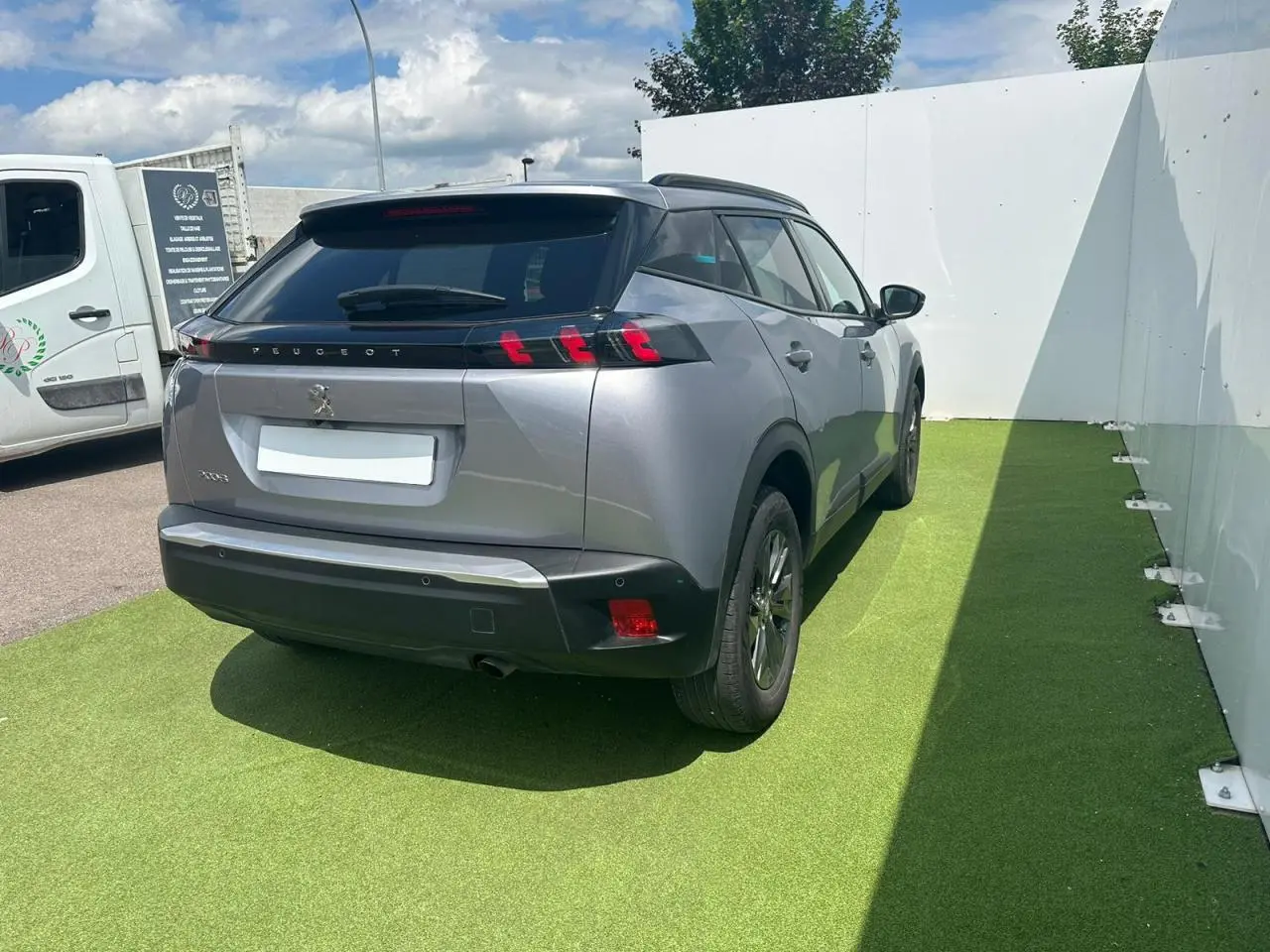 Vue 3/4 arrière droite d'un Peugeot 2008 gris clair avec feux arrière à trois griffes et toit noir brillant.