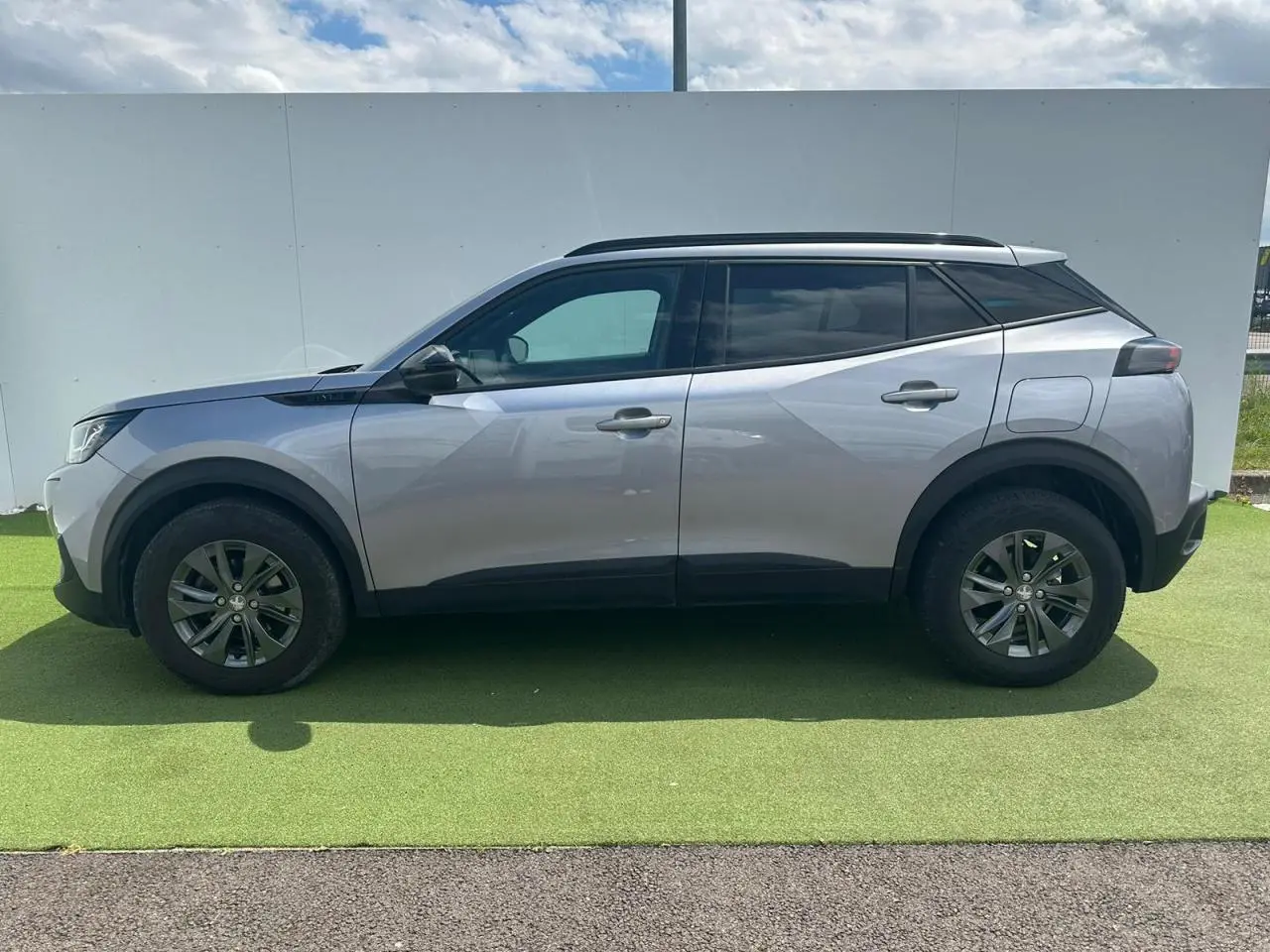 Profil côté gauche du Peugeot 2008 gris clair de 2022 avec jantes alliage et barres de toit noires.