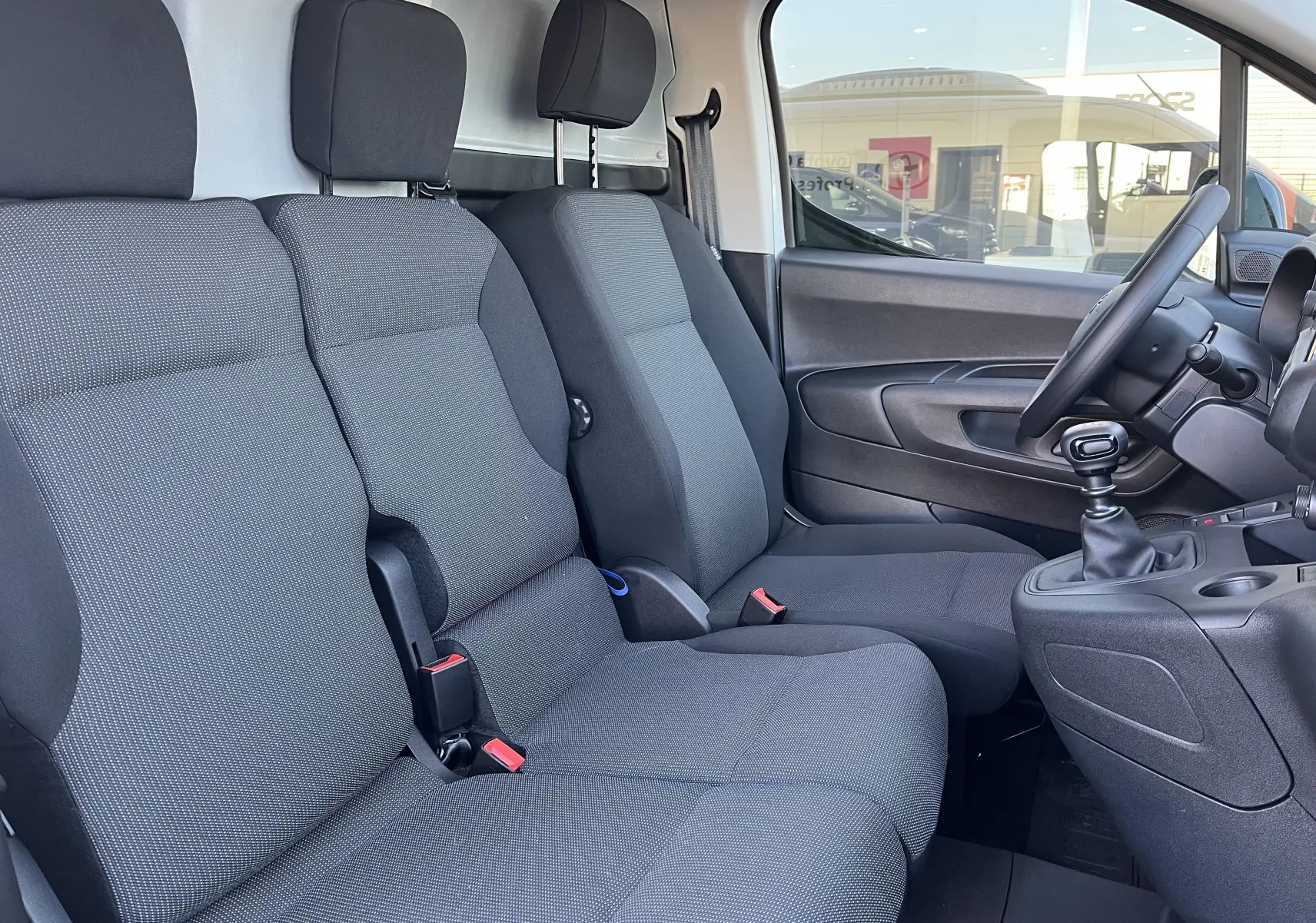 Vue intérieure côté conducteur du Toyota Proace City blanc glacier 2023, montrant les sièges avant et le levier de vitesses manuel.