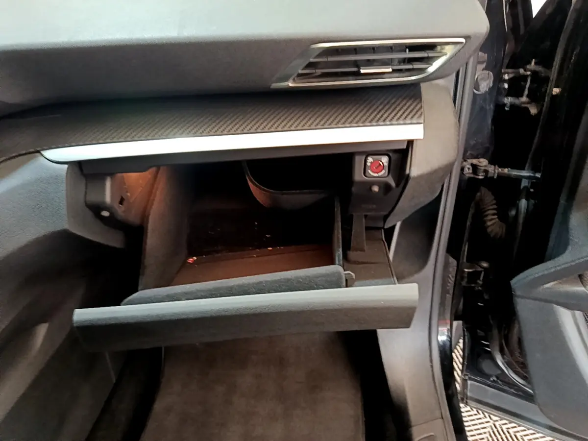 Intérieur du Peugeot 3008 noir, vue côté passager avec boîte à gants ouverte et tableau de bord en carbone.
