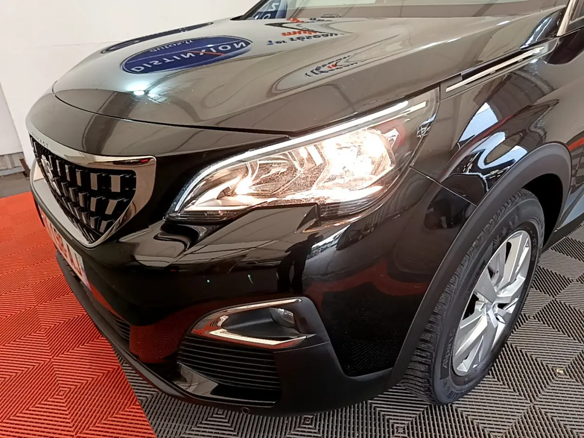 Vue 3/4 avant droit du Peugeot 3008 noir avec phares allumés et jante alliage visible.