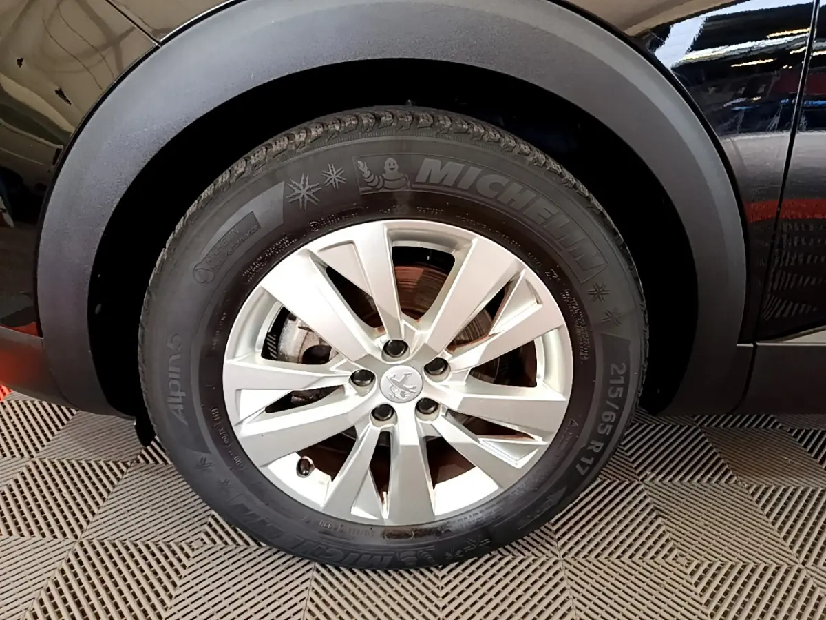 Gros plan sur la roue avant gauche d’un Peugeot 3008 noir, mettant en valeur la jante alliage et le pneu Michelin hiver.