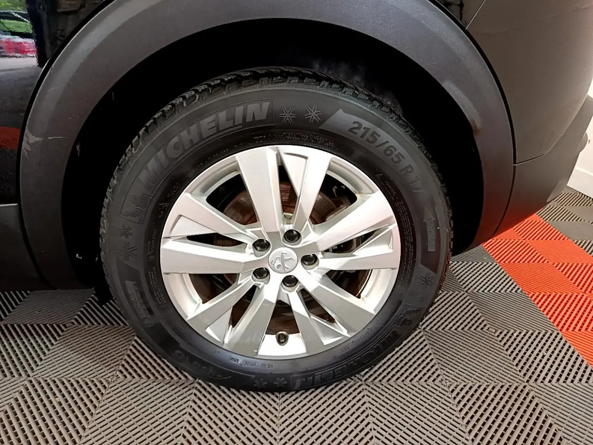 Gros plan sur la roue avant droite d’un Peugeot 3008 noir, jante alliage argentée et pneu Michelin visible.