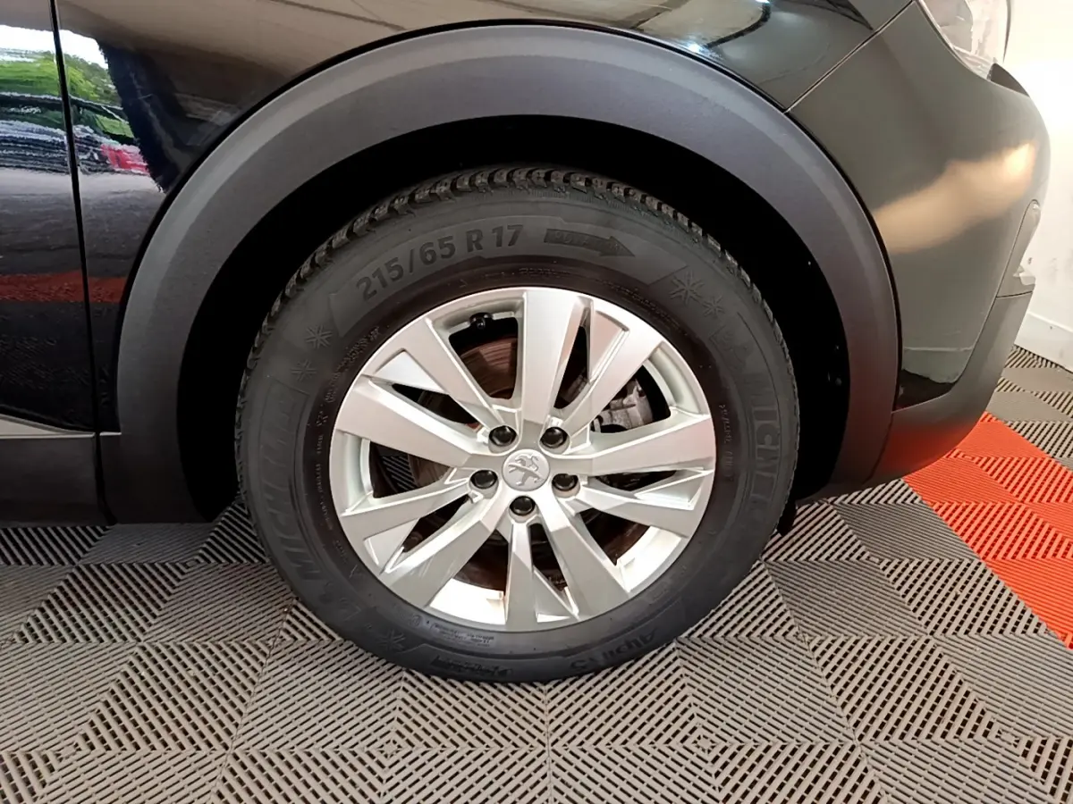 Gros plan sur la roue avant droite noire d’un Peugeot 3008 2019 avec jante argentée et logo lion central.
