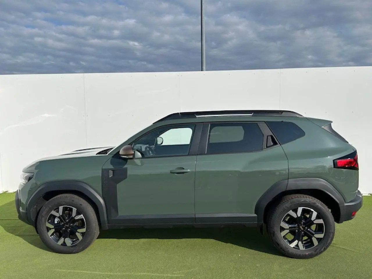 Profil côté gauche du Dacia Duster III 1.6 Hybrid 140 4x2 en kaki dusty avec jantes alliage et barres de toit noires.