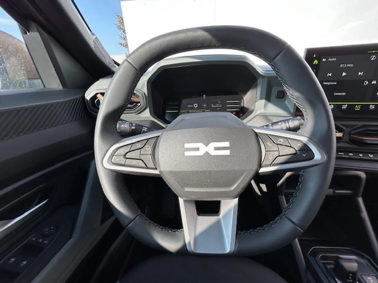 Vue intérieure centrée sur le volant noir du Dacia Duster III 1.6 Hybrid 140 4x2 Extreme avec tableau de bord digital.