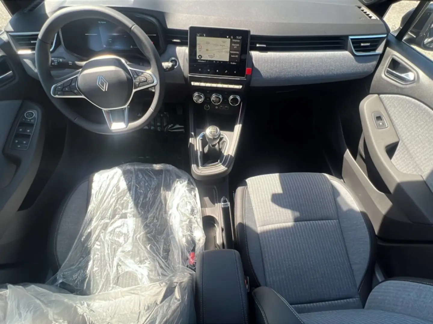Vue intérieure avant de la Renault Clio V 1.0 TCe 90 Techno, sièges gris et volant multifonction noir.