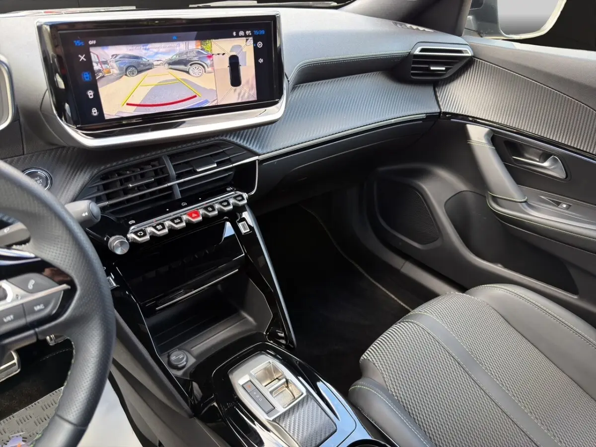 Vue intérieure côté passager du tableau de bord et console centrale noire avec écran tactile et volant cuir partiel du Peugeot 2008 Hybrid 145 GT.
