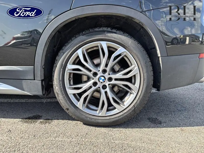 Gros plan sur la roue arrière droite d'un BMW X1 xDrive25eA 220ch saphirschwarz avec jante alu distinctive.