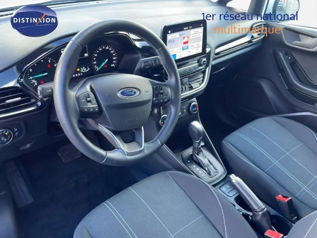 Vue intérieure avant droite de la Ford Fiesta 2020, montrant le volant, la console centrale avec écran tactile et la sellerie tissu noire.