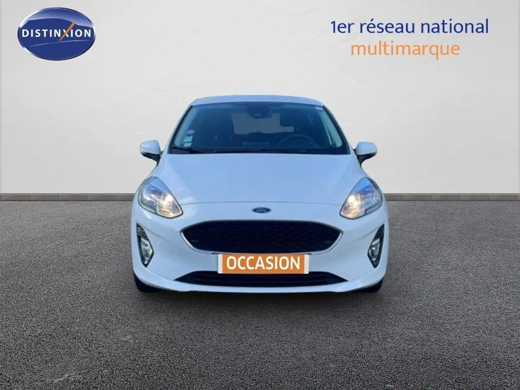 Vue frontale d'une Ford Fiesta blanche 2020 avec phares allumés et plaque "OCCASION" visible.