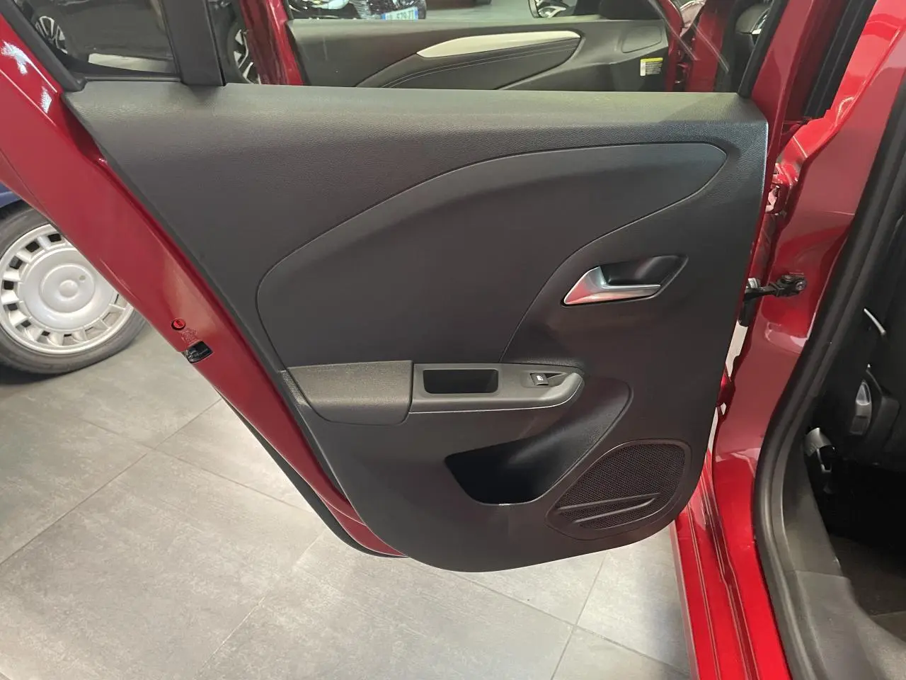 Vue rapprochée de la porte arrière gauche rouge d’une Opel Corsa 2026 avec panneau intérieur noir et poignée argentée.