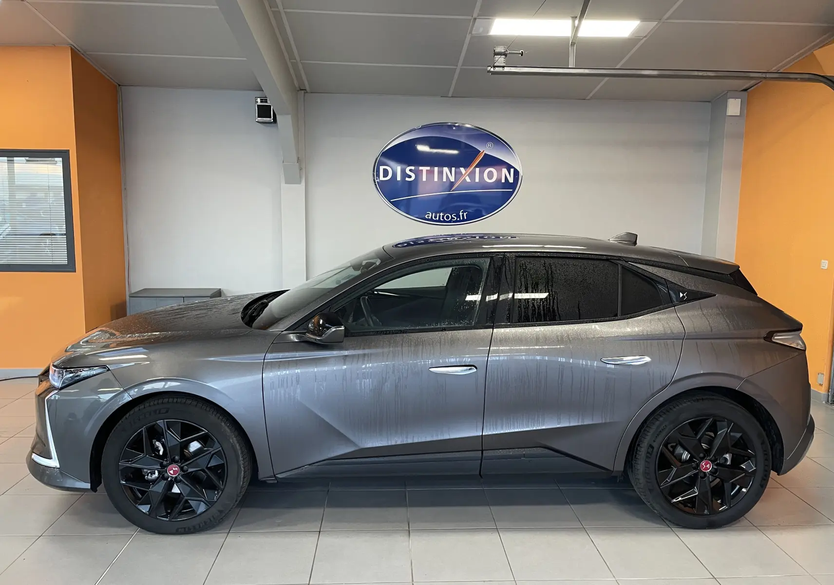 Profil côté gauche de la DS4 2024 gris platinium avec jantes alliage noires 19'' Minneapolis en intérieur showroom.