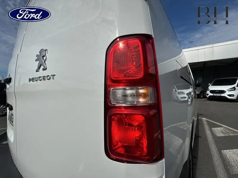 Gros plan sur le feu arrière droit d’un Peugeot Expert Fourgon blanc Banquise, avec reflet du véhicule sur le côté.