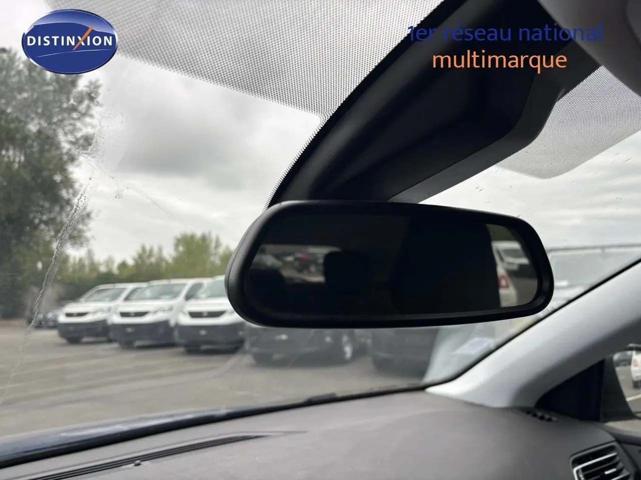 Vue intérieure du rétroviseur central d'une Peugeot 308 Bleu Magnetic, avec un parking en arrière-plan flou.