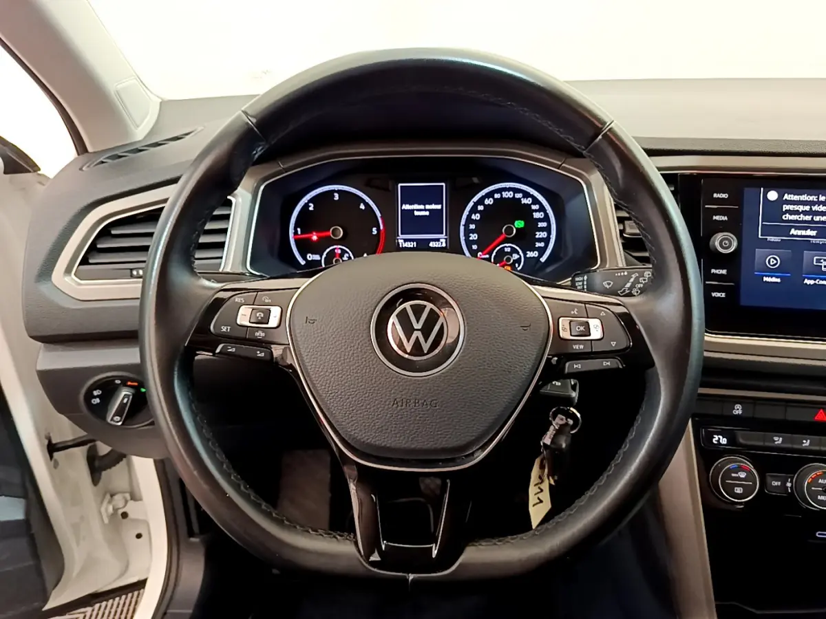Vue frontale du volant cuir noir et tableau de bord numérique du Volkswagen T-Roc blanc 2021 avec écran tactile central.