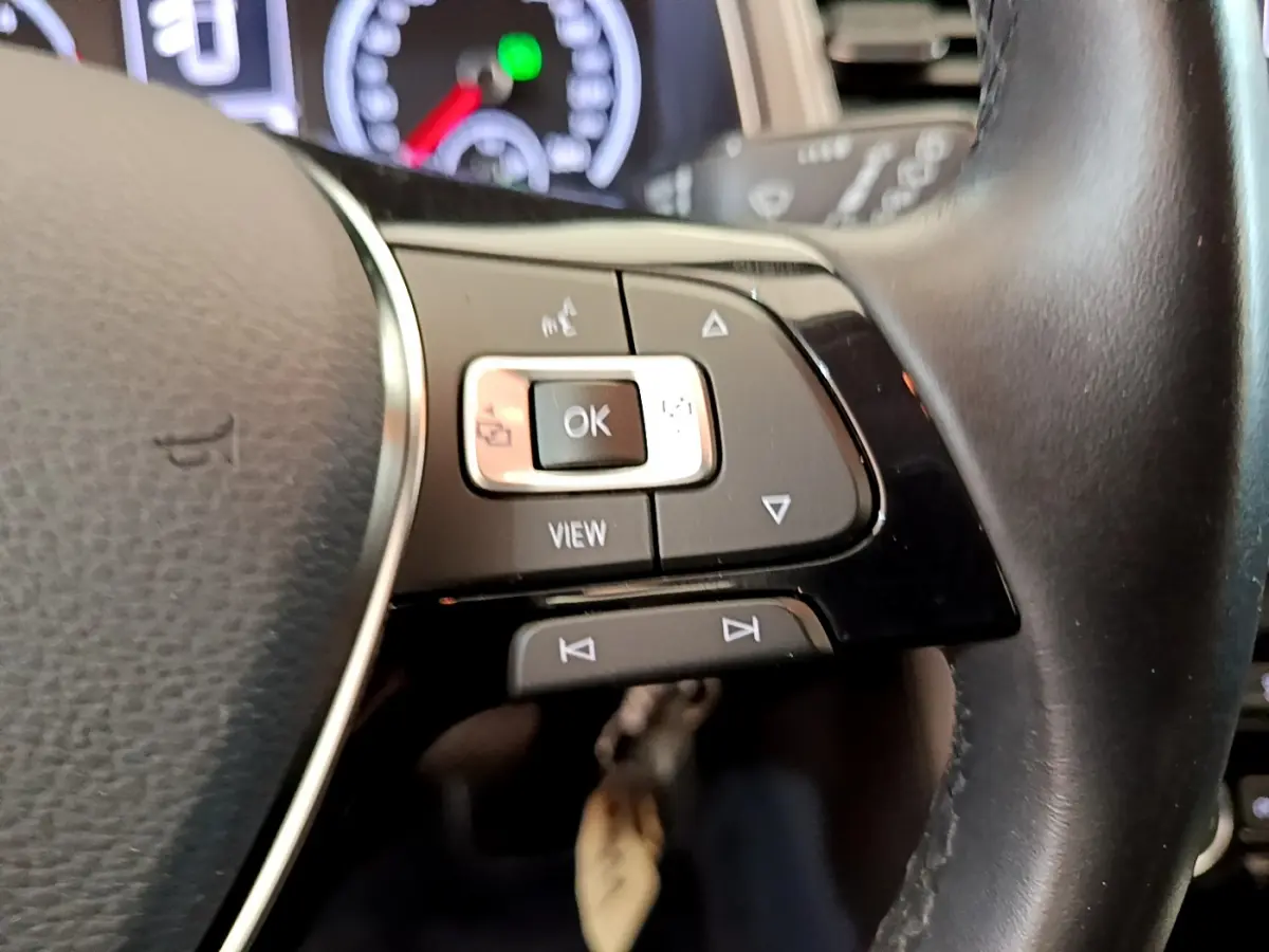 Gros plan sur les commandes multifonctions du volant cuir du Volkswagen T-Roc, avec tableau de bord numérique en arrière-plan.