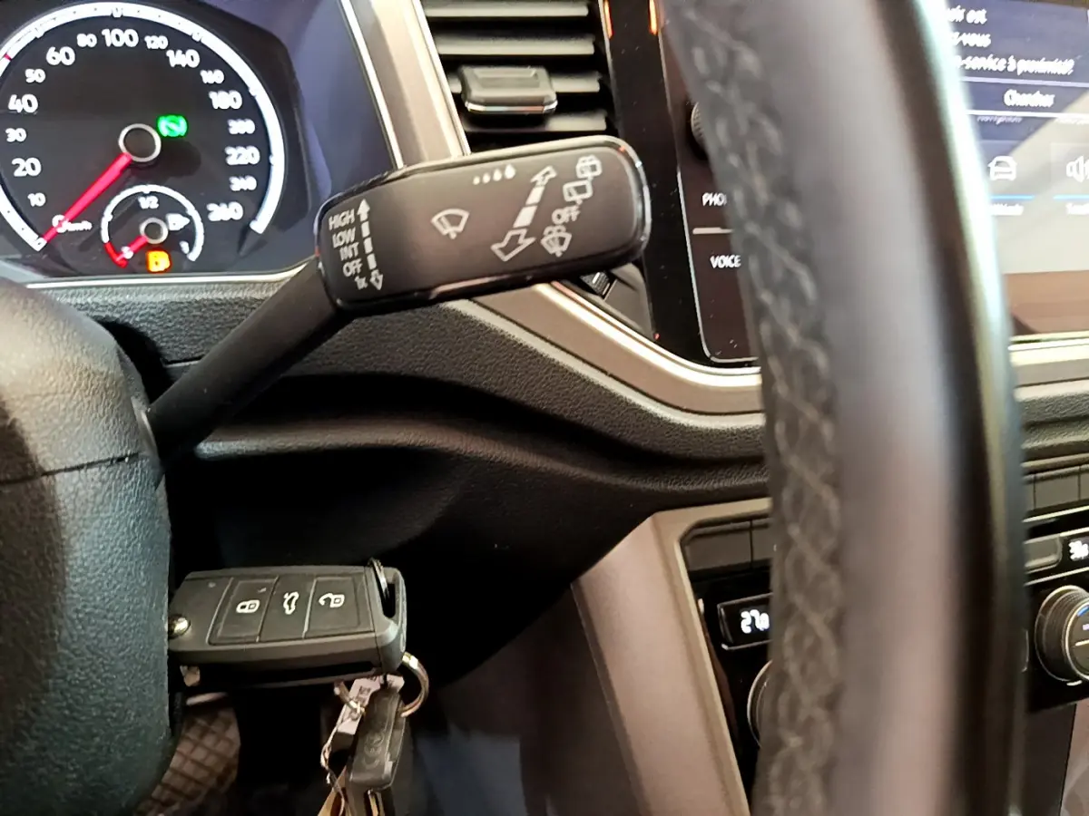 Gros plan sur la manette d’essuie-glace et le tableau de bord du Volkswagen T-Roc blanc, avec clé insérée.
