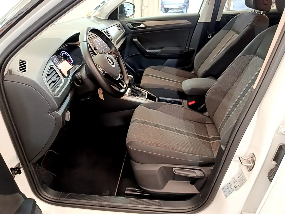 Intérieur avant droit d'un Volkswagen T-Roc blanc 2021, sièges tissu gris et tableau de bord avec écran tactile.