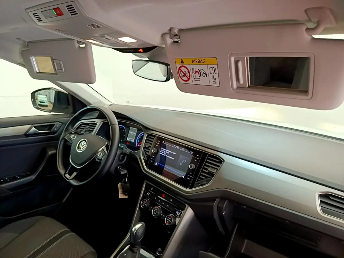 Intérieur du Volkswagen T-Roc blanc 2021 vu côté conducteur, tableau de bord avec écran tactile et volant multifonctions cuir.